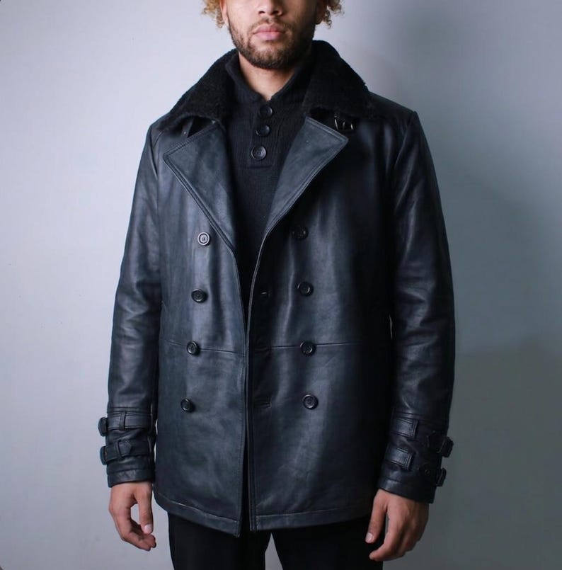 May include: A dark blue leather jacket with a double-breasted design. The jacket features a black faux fur collar, multiple buttons, and buckle details on the sleeves. The jacket is a classic style.