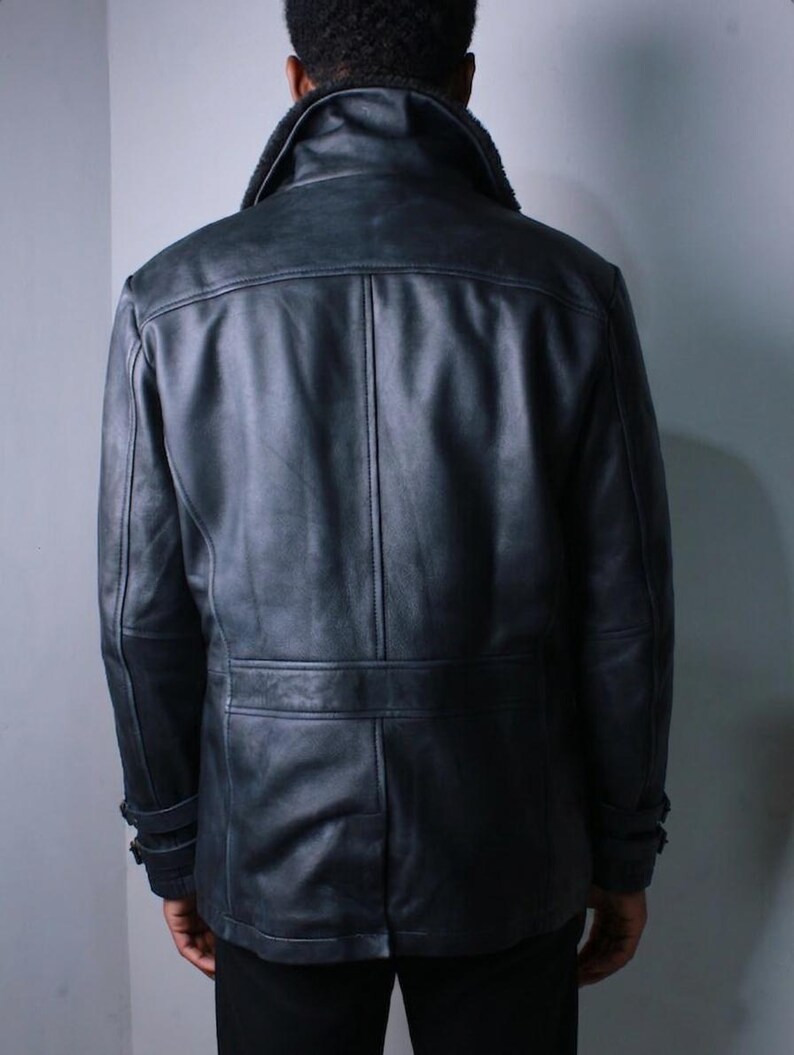 May include: A black leather jacket with a shearling collar. The jacket has a double-breasted design with a belt detail at the waist and buttoned cuffs. The jacket is worn by a person.