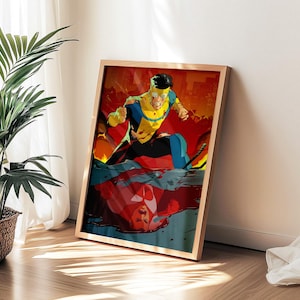 May include: A framed art print featuring a superhero in a dynamic pose, clad in a yellow and blue costume, set against a vibrant red and orange background. The artwork is displayed on a wooden floor next to a potted plant.