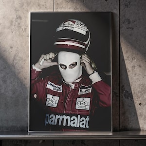 May include: Framed print of a Formula 1 driver in a red racing suit and white balaclava, adjusting their helmet. The helmet displays "Marlboro" and "Parmalat" branding. The image is set against a dark background.