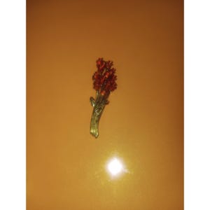 May include: A gold-toned brooch in the shape of a bouquet of flowers. The flowers are a deep red color, and the stems and leaves are gold. The brooch is likely made of metal and is designed to be worn as an accessory.