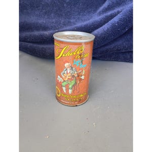 May include: Vintage Schells Export Light Beer can. The can has a brown background with a cartoon image of a man playing a guitar. The can reads "August Schell Brewing Co. New Ulm, Minn." and "Contents 12 fl. oz."