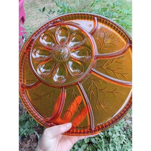 May include: A round amber-colored glass serving tray featuring a central circular section with a pressed flower petal design surrounded by three larger partitioned compartments decorated with embossed leaf patterns and a beaded outer rim edge.