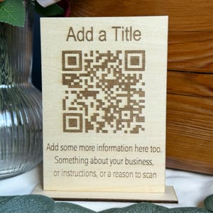 May include: A light-coloured wooden sign featuring the text "Add a Title" and a QR code. The text below the QR code reads "Add some more information here too. Something about your business, or instructions, or a reason to scan."