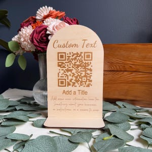 Peut inclure: Panneau en bois clair avec un dessus en forme d'arche. Le panneau comporte un code QR et les mots "Custom Text" et "Add a Title". En dessous du titre se trouve le texte : "Add some more information here too. Something about your business, or instructions, or a reason to scan."
