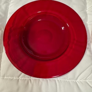 May include: A vibrant red glass plate with a glossy finish. The plate has a wide rim and a slightly recessed center. The color is a deep, rich shade of red, perfect for serving food or as a decorative piece.