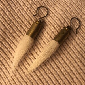 May include: A pair of earrings made from brass bullet casings with white horsehair tassels.