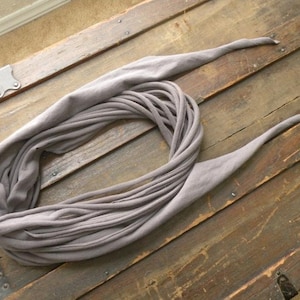 May include: A gray fabric scarf made from a long strip of fabric twisted and tied into a loop.