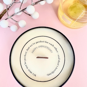 May include: A white candle with a black rim and a message that reads "We may not be perfect, but we're perfect for each other. Happy Anniversary and that's terrifying."