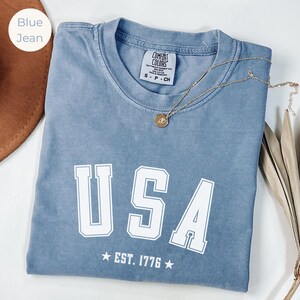 Camiseta com letras do time universitário dos EUA em cores confortáveis | Camiseta patriótica vintage unissex | Camiseta do 4 de julho | Camiseta EUA EST 1776 | Camiseta com estampa da bandeira americana