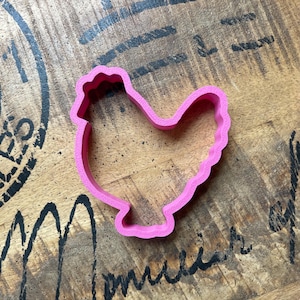 May include: Pink plastic cookie cutter shaped like a chicken.