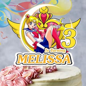 May include: A cake topper featuring a Sailor Moon character illustration, a large yellow number 3, and the text "Is Turning MELISSA" in yellow and white. The topper is positioned on a round cake with pink frosting rosettes and sprinkles.
