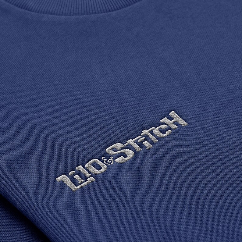 May include: A navy blue t-shirt with a white embroidered logo that reads "Lilo & Stitch".