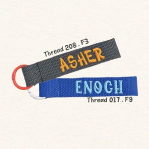 May include: Two personalized keychains. One is gray with the name "ASHER" in orange thread, attached to a red ring. The other is blue with "ENOCH" in blue thread. The text "Thread 208, F3" and "Thread 017, F9" are also visible.