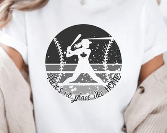 Op de afbeelding: Wit T-shirt met een zwart-witte afbeelding van een honkballer met een Canadese vlag op zijn shirt. De afbeelding bevindt zich in een cirkel met de tekst "There's no place like HOME".