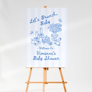 Peut inclure: Un chevalet en bois présente une affiche à rayures bleues et blanches. L'affiche présente des illustrations bleues d'éléments de brunch et le texte "Let's Brunch, Baby - Welcome to Vivienne's Baby Shower."
