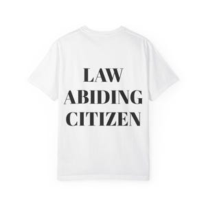 Può includere: T-shirt bianca con la scritta "LAW ABIDING CITIZEN" stampata in nero sul retro. Il testo è in grassetto, con un carattere sans-serif. La maglietta è realizzata in un materiale morbido e opaco.