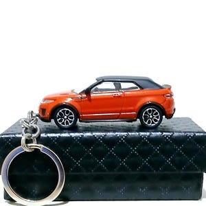 Könnte beinhalten: Ein Miniatur-SUV-Cabrio-Schlüsselanhänger mit schwarzem Dach, silberfarbenen Rädern und einem metallenen Schlüsselring. Das Fahrzeugmodell wird im Profil gezeigt und präsentiert sein kompaktes Design sowie die detaillierte Lackierung.