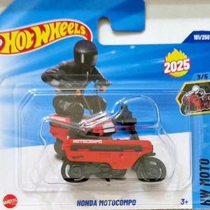 May include: A red Honda Motocompo toy motorcycle with a black rider in a black helmet and suit. The toy is in a clear plastic package with the Hot Wheels logo and the text "2025". The package also has the text "HW Moto".