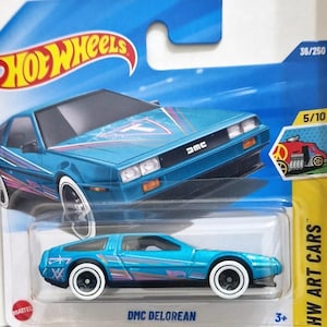 May include: A blue DMC DeLorean toy car with white-rimmed wheels, part of the Hot Wheels Art Cars series. The car has a futuristic design with pink and purple accents. The packaging includes the Hot Wheels logo and the text "DMC DeLorean".