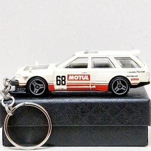 May include: White and red die-cast model car keyring. The car features the number 68 and the word "MOTUL" on the side. The keyring has a silver ring and chain. The car is approximately 7.6 cm long.