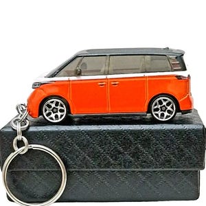 May include: A black and orange toy car keychain with a silver key ring. The car is a van with a white stripe and black wheels.