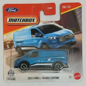 May include: A Matchbox toy car of a 2023 Ford E-Transit Custom van. The die-cast model is blue with white accents and the text "E" and "TRANSIT". The packaging includes the Ford and Matchbox logos, and the text "36/125".