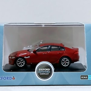 Könnte beinhalten: Ein rotes Jaguar XF Modellauto in einer Präsentationsbox. Das Modell hat schwarze Räder und ein schlankes Design. Die Box zeigt das Logo "Oxford Automobile Company" und einen Maßstab von 1:76.