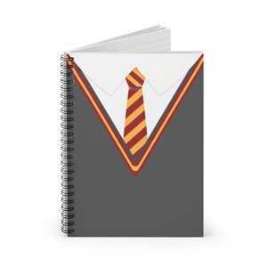 May include: A spiral-bound notebook with a design resembling a school uniform. The cover features a gray sweater, a white collared shirt, and a yellow and red striped tie. The notebook is open, revealing blank white pages.