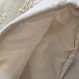 May include: A white fabric pouch with a folded edge, showing the inside of the pouch. The fabric has a delicate embroidered design.