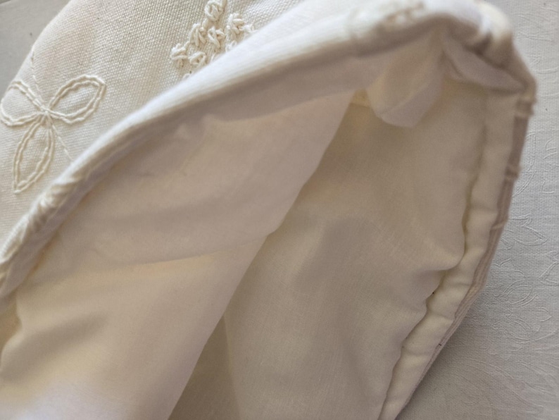 May include: A white fabric pouch with a folded edge, showing the inside of the pouch. The fabric has a delicate embroidered design.