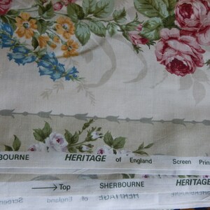 Puede incluir: Primer plano de una tela beige con un patr&oacute;n floral con rosas rosas, flores amarillas y campanillas. La tela tiene un borde blanco con el texto "SHERBOURNE HERITAGE of England Screen Printed Fabric" repetido.
