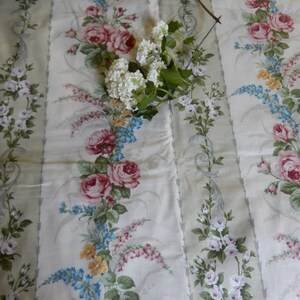 Puede incluir: Tela blanca con un patr&oacute;n repetido de rosas rosas y blancas, flores azules y amarillas y hojas verdes. La tela tiene un fondo a rayas.