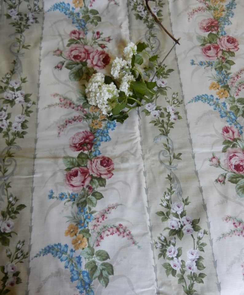Puede incluir: Tela blanca con un patr&oacute;n repetido de rosas rosas y blancas, flores azules y amarillas y hojas verdes. La tela tiene un fondo a rayas.