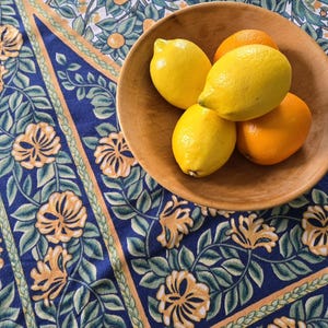 May include: A wooden bowl filled with lemons and oranges. The bowl is on a blue and yellow floral tablecloth.