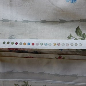 Puede incluir: Primer plano de una tela blanca con una fila de peque&ntilde;os c&iacute;rculos coloridos. Los c&iacute;rculos son en tonos de verde, rojo, naranja, amarillo, azul y rosa. La tela tiene un sutil estampado floral.