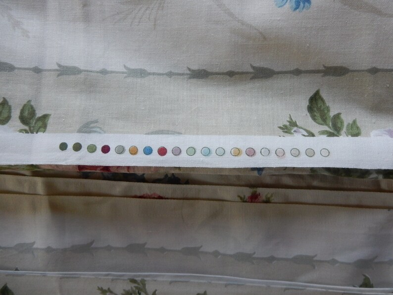 Puede incluir: Primer plano de una tela blanca con una fila de peque&ntilde;os c&iacute;rculos coloridos. Los c&iacute;rculos son en tonos de verde, rojo, naranja, amarillo, azul y rosa. La tela tiene un sutil estampado floral.