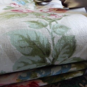 Puede incluir: Primer plano de una tela doblada con un patr&oacute;n floral. La tela es blanca con hojas verdes y flores rosas. Una cinta gris es visible en el lado derecho de la imagen.