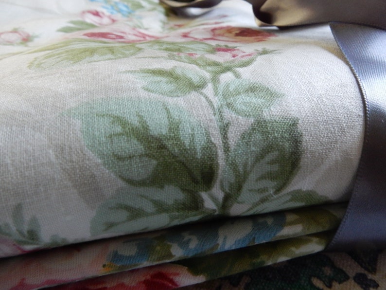 Puede incluir: Primer plano de una tela doblada con un patr&oacute;n floral. La tela es blanca con hojas verdes y flores rosas. Una cinta gris es visible en el lado derecho de la imagen.