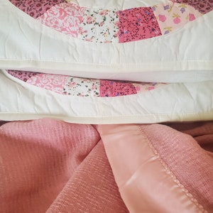 May include: A pink and white patchwork quilt with a floral pattern. The quilt is folded in half and the top layer is pulled back to reveal the bottom layer.