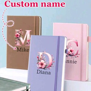 Op de afbeelding: Gepersonaliseerde notitieboeken in bruin, lavendel en roze. Elk notitieboek heeft een bloemen beginletter en een naam. De tekst "Custom name" staat bovenaan de afbeelding.