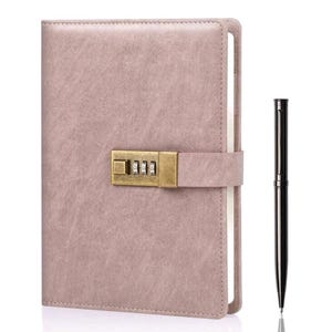 Puede incluir: Un diario de color rosa polvoriento con cerradura de combinación y un bolígrafo a juego. El diario tiene una cubierta texturizada y un cierre de correa. El bolígrafo es negro y tiene una punta plateada. El diario es un cuaderno.