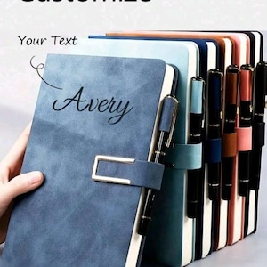 May include: A collection of personalized notebooks in various colors, including blue, teal, brown, and pink. The notebooks feature a pen holder and a gold-colored clasp. The word "Customize" and "Your Text" are displayed at the top, with the name "Avery" on the front of the blue notebook.
