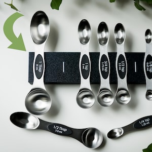 Könnte beinhalten: Ein Set aus Edelstahl-Messlöffeln und einem Abstreifer. Die Löffel sind mit Maßen wie 1 Esslöffel (15 ml), 1 Teelöffel (5 ml) und 1/4 Teelöffel (1,25 ml) beschriftet. Einige Löffel haben schwarze Griffe. Der Abstreifer ist silberfarben.