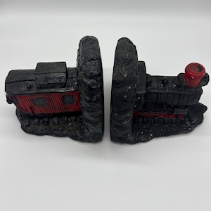 以下が含まれることがあります： 赤色のアクセントが付いた黒い列車のブックエンド。ブックエンドは、詳細な成形と質感のある風化した外観を備えた、ヴィンテージの機関車のような形をしています。列車の車両には赤いカブースと赤い煙突があります。