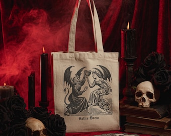 May include: Beige tote bag with a black and white illustration of a devil and angel toasting. The text "Hell's Brew" is below the illustration. The background includes black candles, roses, a skull, and tarot cards on a red velvet surface.