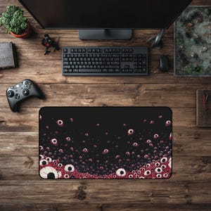 May include: Black rectangular mouse mat with a graphic of many red and white eyeballs on a black background. A keyboard, monitor, and other gaming accessories surround the mat on a wooden surface.