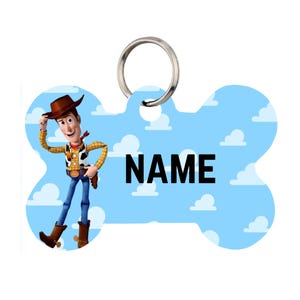 Puede incluir: Una etiqueta para mascotas en forma de hueso con el personaje Woody de Toy Story. La etiqueta tiene un fondo azul claro con nubes blancas y la palabra "NAME". Un anillo plateado está adjunto para una fácil fijación al collar de una mascota.
