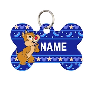 Könnte beinhalten: Ein blauer, knochenförmiger Haustieranhänger mit einem Cartoon-Chipmunk-Charakter und dem Wort "NAME" in Weiß. Der Anhänger hat einen silbernen Ring zur Befestigung und ein Muster aus Sternen und Mickey-Mouse-Silhouetten.