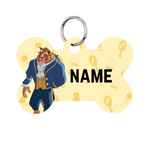 May include: Bone-shaped pet tag featuring an illustration of the Beast from Beauty and the Beast. The tag is yellow with a pattern of roses and mirrors. The word "NAME" is printed in black.